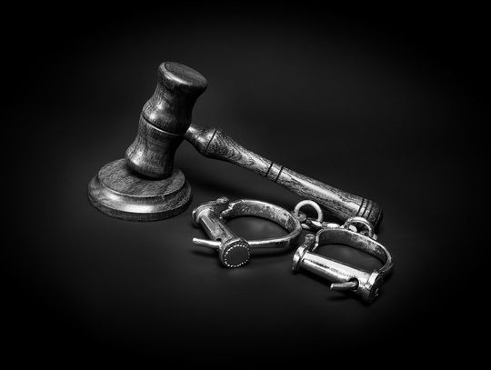 Black and white stock image of a judge's gavel and a pair of old-fashioned handcuffs set against a black background