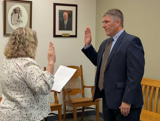 Photo of David Sigler, a white man in his 40s wearing a dark blue suit, light blue shirt and brown tie standing with his right hand raised as he takes the oath of office in the Lexington City Circuit Court Clerk's office