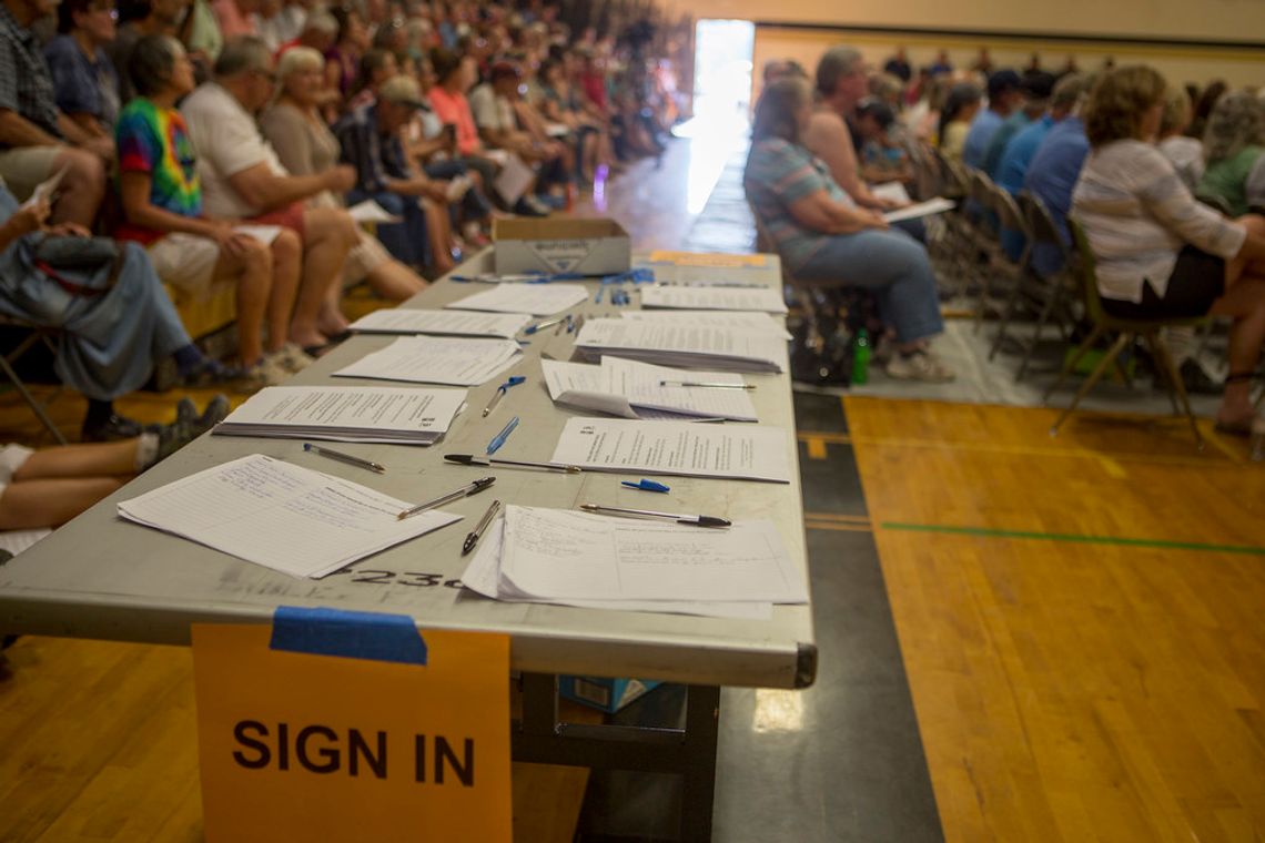 Lexington City, School Staff To Host Conversations About Proposed Sales Tax Referendum photo of a gymnasium where a public meeting is being held. In the foreground, a rectangular table with several stacks of papers and pens scattered upon it with a sign saying "SIGN IN" in all capital large black letters on orange paper is taped to the table. Several rows of people in the background